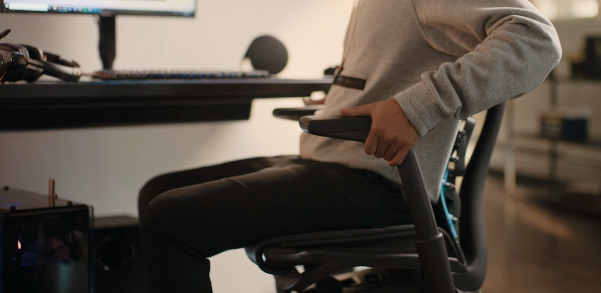 特写视频：桌子前的一个人正在调整黑色Embody电竞椅的扶手。