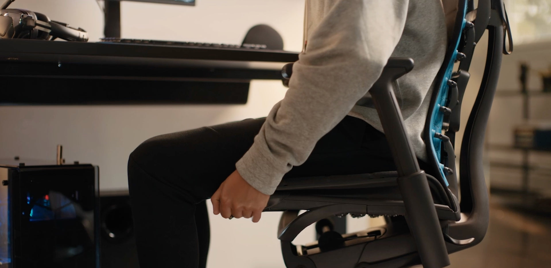 特写视频：一个穿着运动衫和长裤的人正在调整黑色Embody电竞椅侧面的座椅深度调节机制